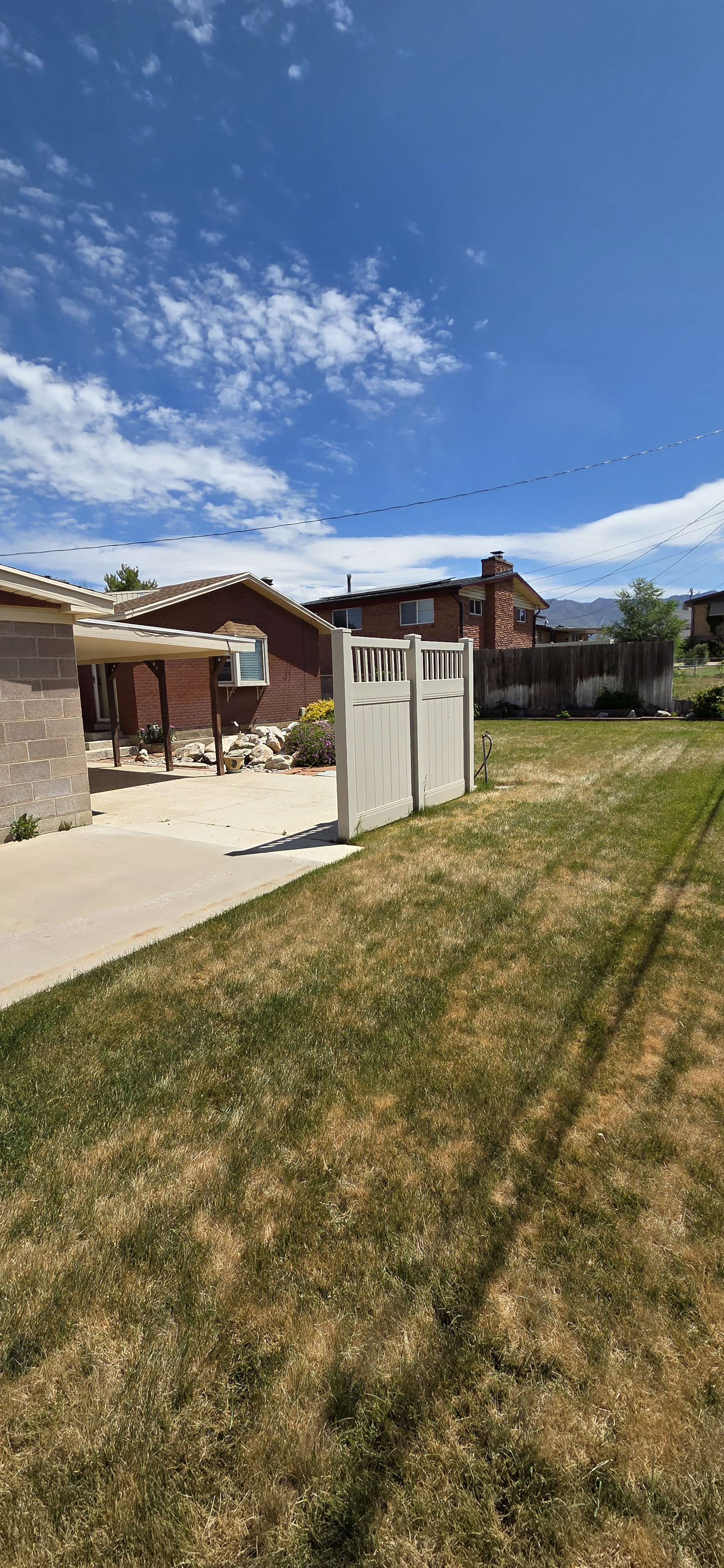 Expansive backyard featuring a concrete patio, a section of lawn, and a light-colored privacy fence