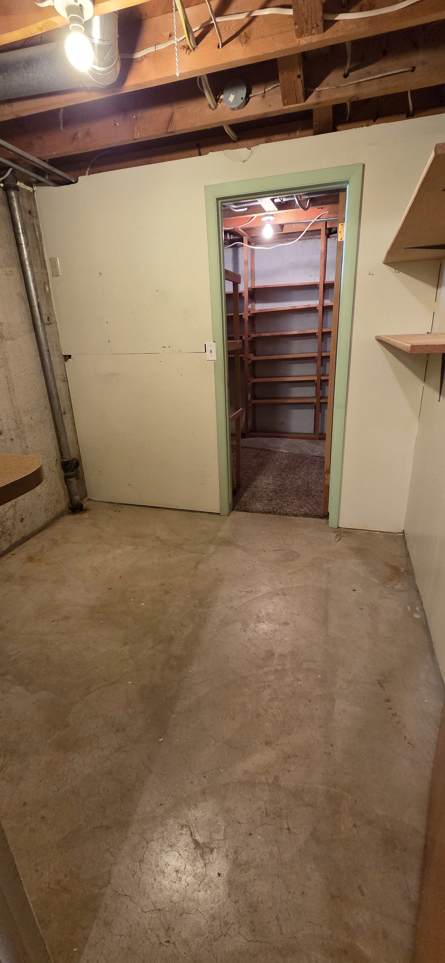 Utility room featuring exposed ceiling joists, concrete flooring, and a doorway to a storage area with built-in shelving