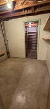 Utility room featuring exposed ceiling joists, concrete flooring, and a doorway to a storage area with built-in shelving