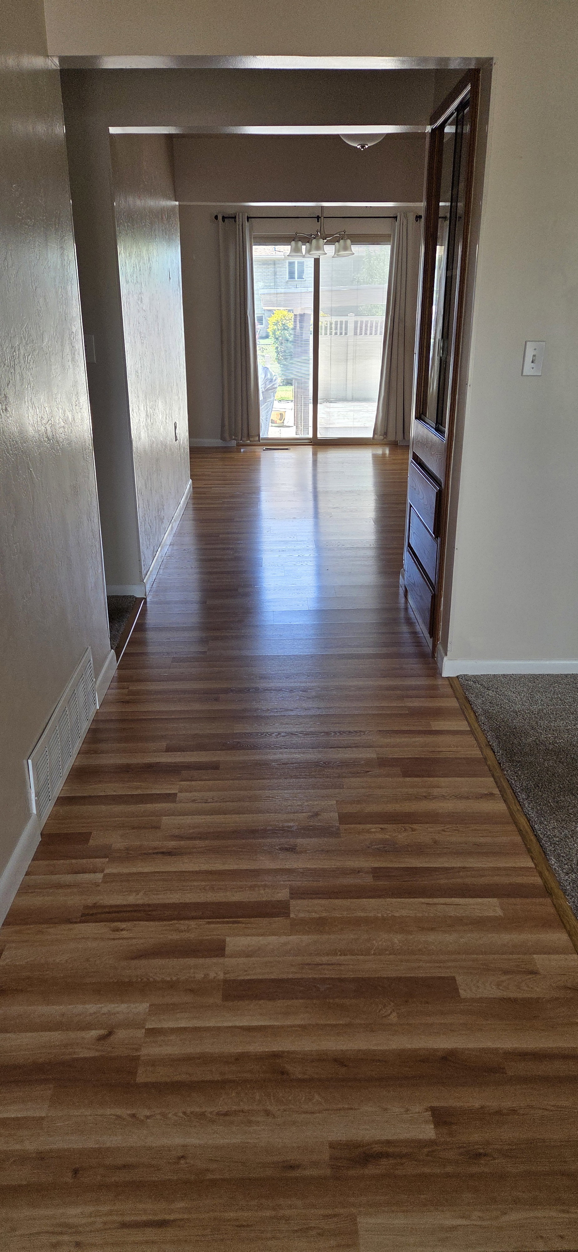 Wood-finish flooring extending from the entryway through to a rear room, featuring sliding glass doors and a view of the outdoor patio