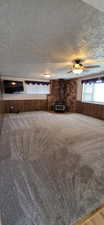 Carpeted room featuring a wood-burning stove with a stone surround, wood paneling, and a ceiling fan with integrated lighting