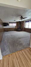 Spacious room featuring gray carpeting, wood-finish wall paneling, and a corner wood-burning stove with a stone surround