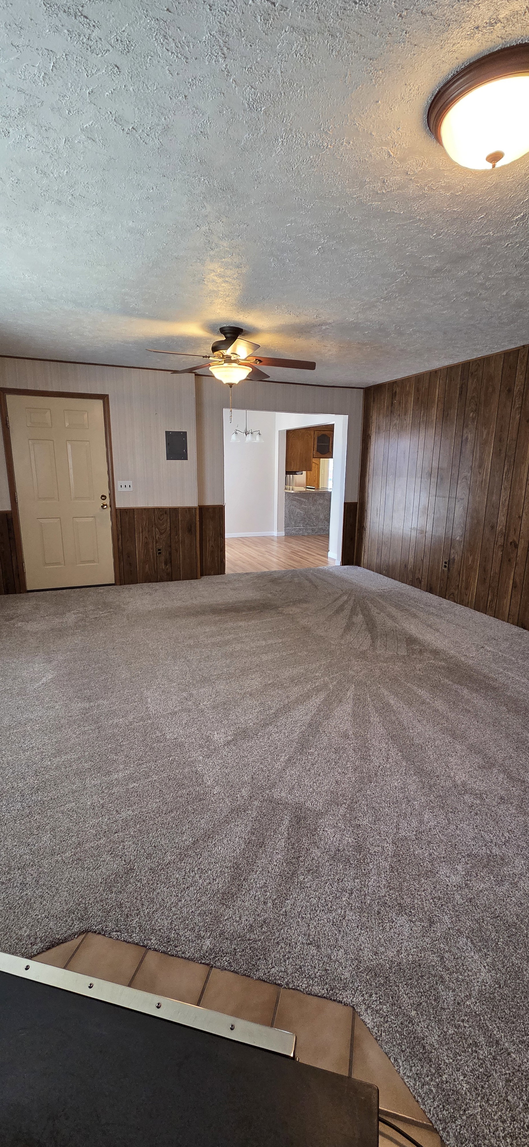 Carpeted living area featuring wood-paneled accent walls and ceiling fan with integrated lighting