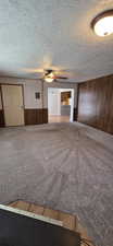Carpeted living area featuring wood-paneled accent walls and ceiling fan with integrated lighting