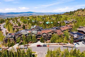 Mountain community featuring a multi-story building with balconies, surrounded by mature trees and paved roads