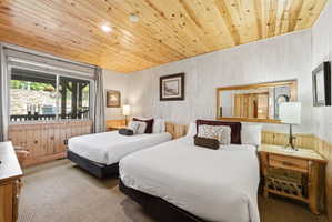 Bedroom featuring two beds with wood-paneled ceilings and wainscoting