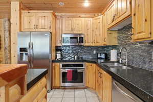 Kitchen featuring wood cabinetry, stainless steel appliances, dark countertops, a mosaic tile backsplash, and recessed lighting