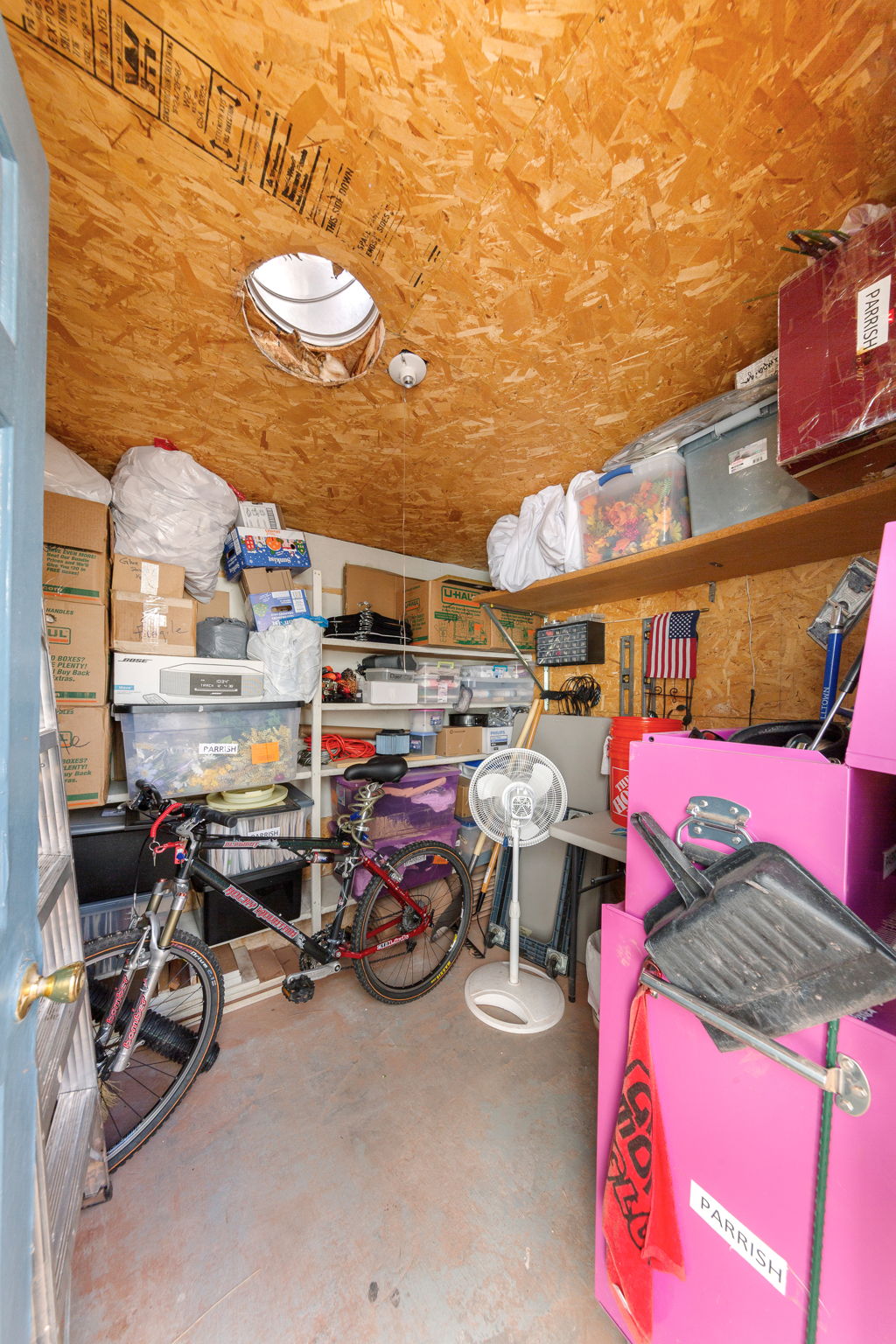 Storage space featuring exposed OSB ceiling and walls, a circular skylight, built-in shelving, concrete flooring, and a solid door