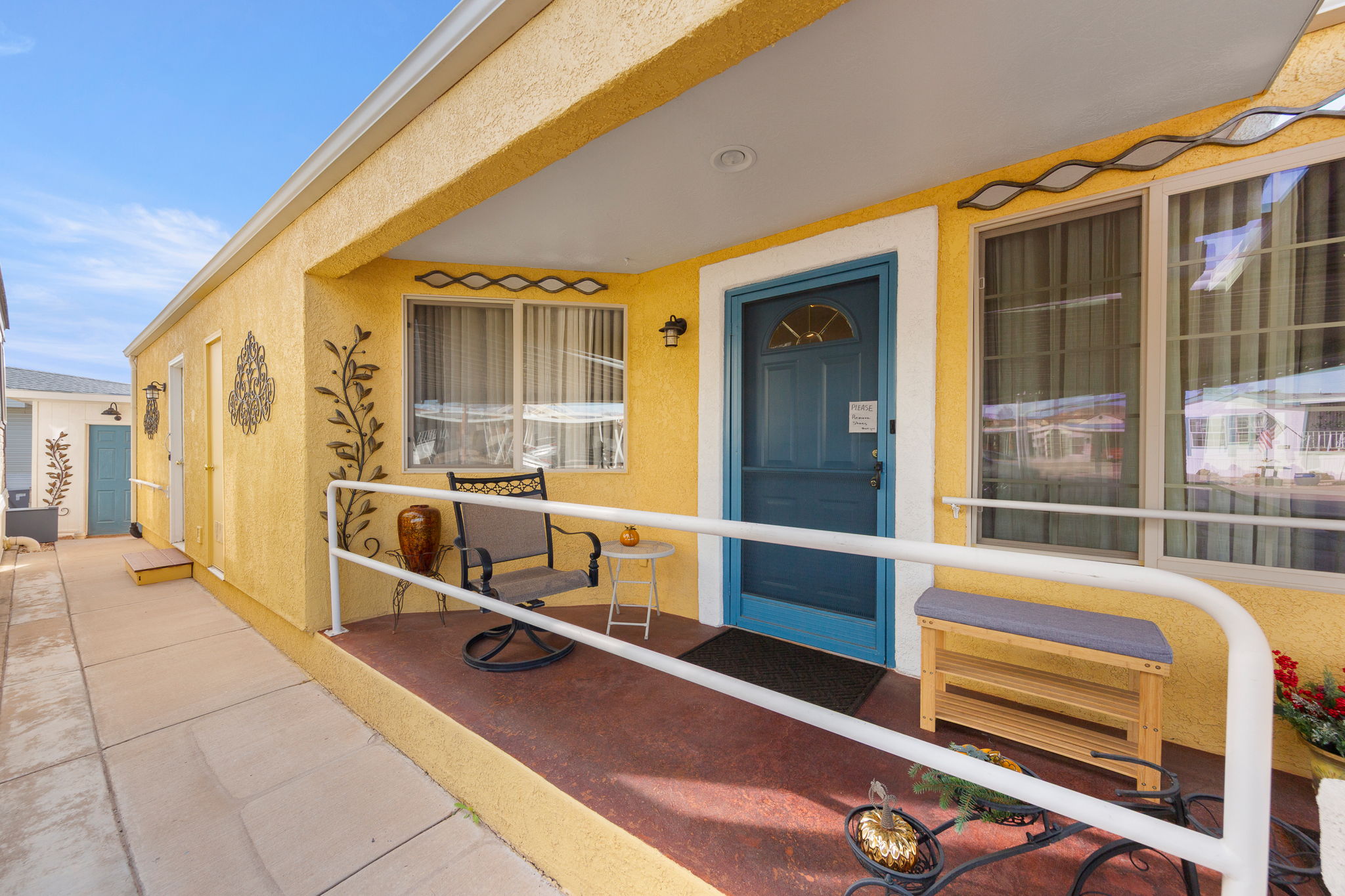 Covered entry with a bright yellow stucco exterior, a blue front door, and a white handrail
