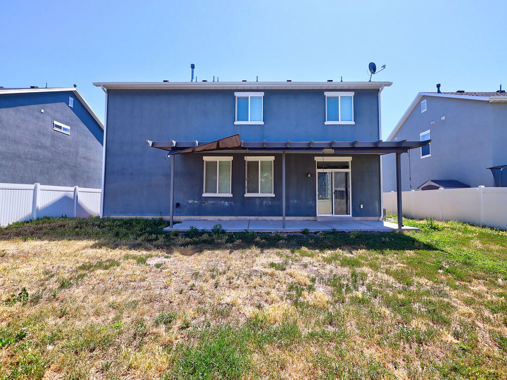 Rear exterior showcasing a ground-level patio with an attached pergola, sliding glass door access, and multiple windows