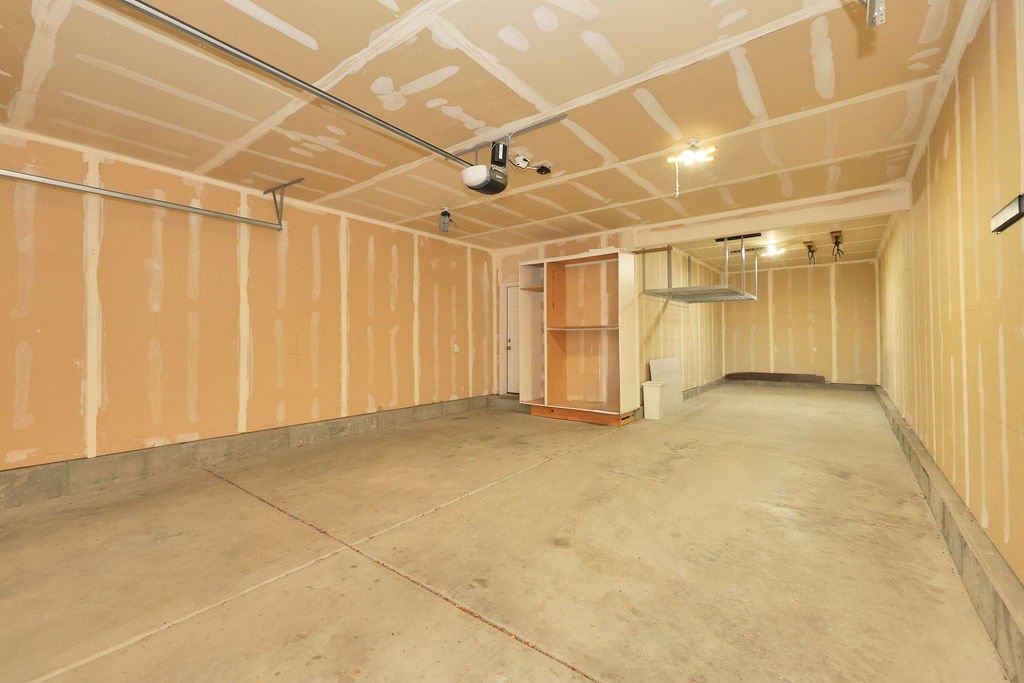 Spacious garage featuring a durable concrete floor, exposed drywall walls, built-in shelving, an automatic garage door opener, and overhead storage racks