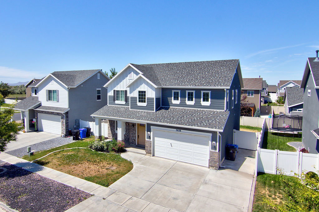 Two-story residence featuring a two-car garage, stone and siding exterior, front porch entry, and a fenced backyard