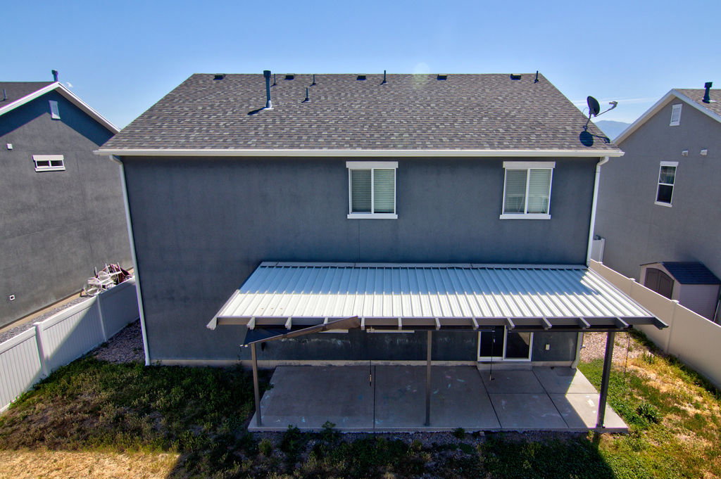 Rear exterior featuring a covered patio with a concrete slab, dark gray stucco siding, and a shingled roof