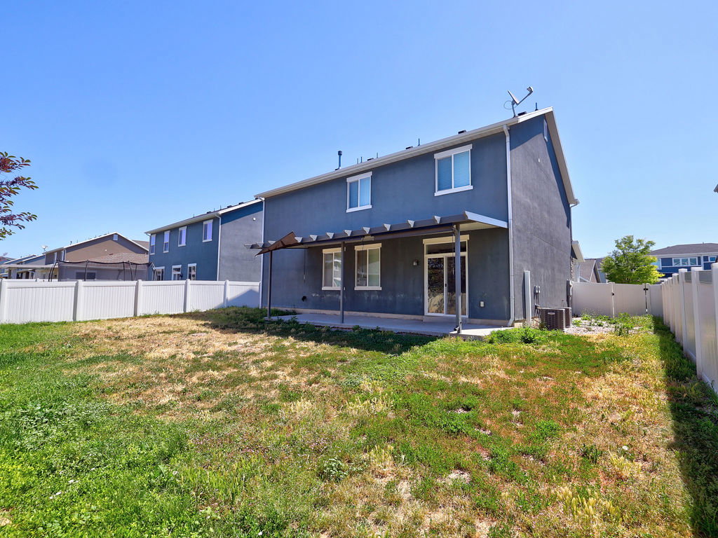 Rear facade featuring a concrete patio with a covered pergola, stucco exterior, and white vinyl fencing