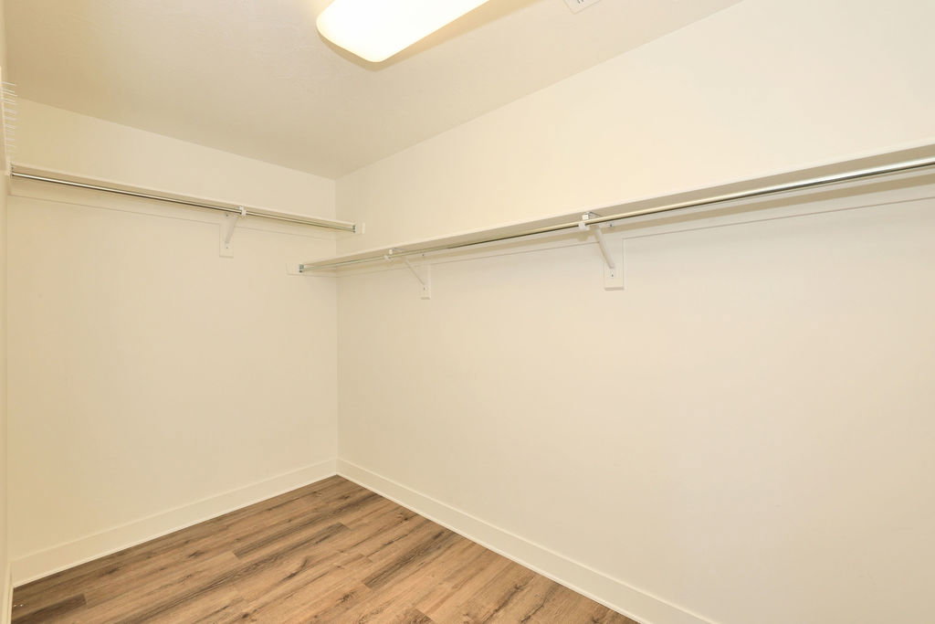 Spacious walk-in closet featuring wood-finish flooring, white walls, white baseboards, and built-in white wire shelving and hanging rods