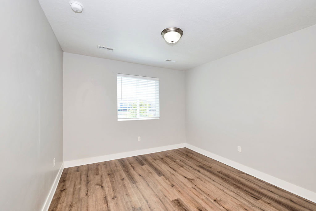 Room featuring wood-finish flooring, light grey painted walls, white baseboards, and a single window with horizontal blinds
