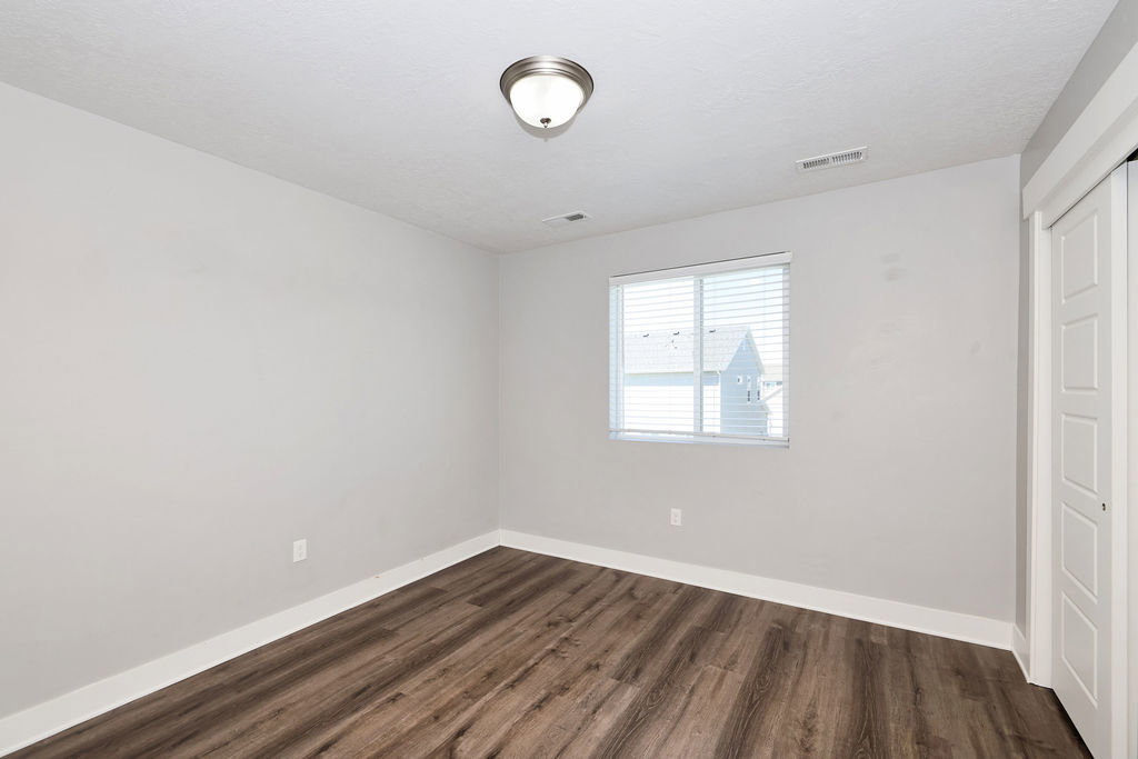 Interior room featuring wood-finish flooring, light-toned walls, and a window with horizontal blinds