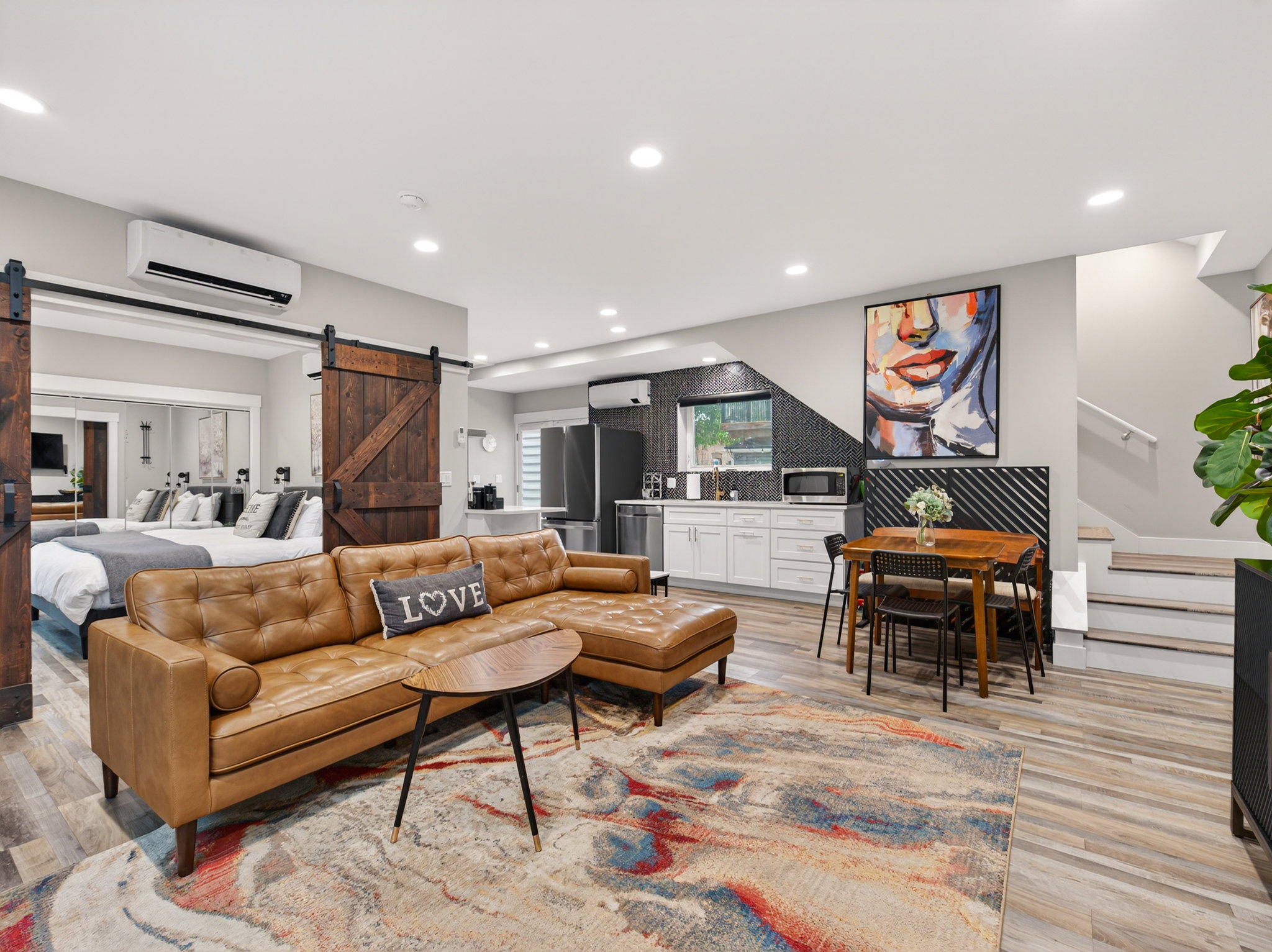 Open-concept living space featuring wood-finish flooring, recessed lighting, and a kitchen area with white cabinetry and black tile backsplash