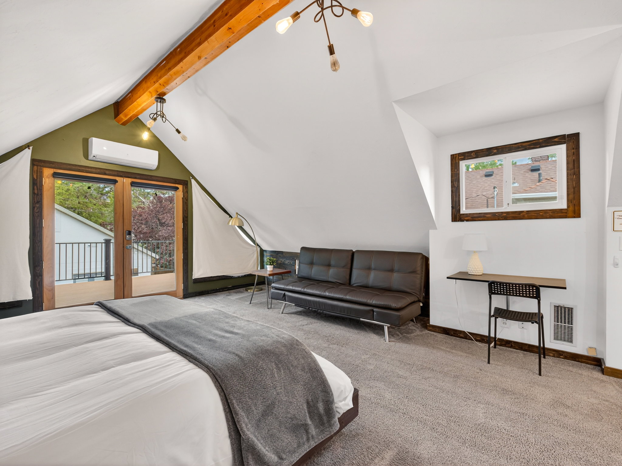 Attic space featuring vaulted ceilings with an exposed wood beam, wood-frame glass doors, a window with wood trim, wall-mounted climate control unit, and gray carpet flooring