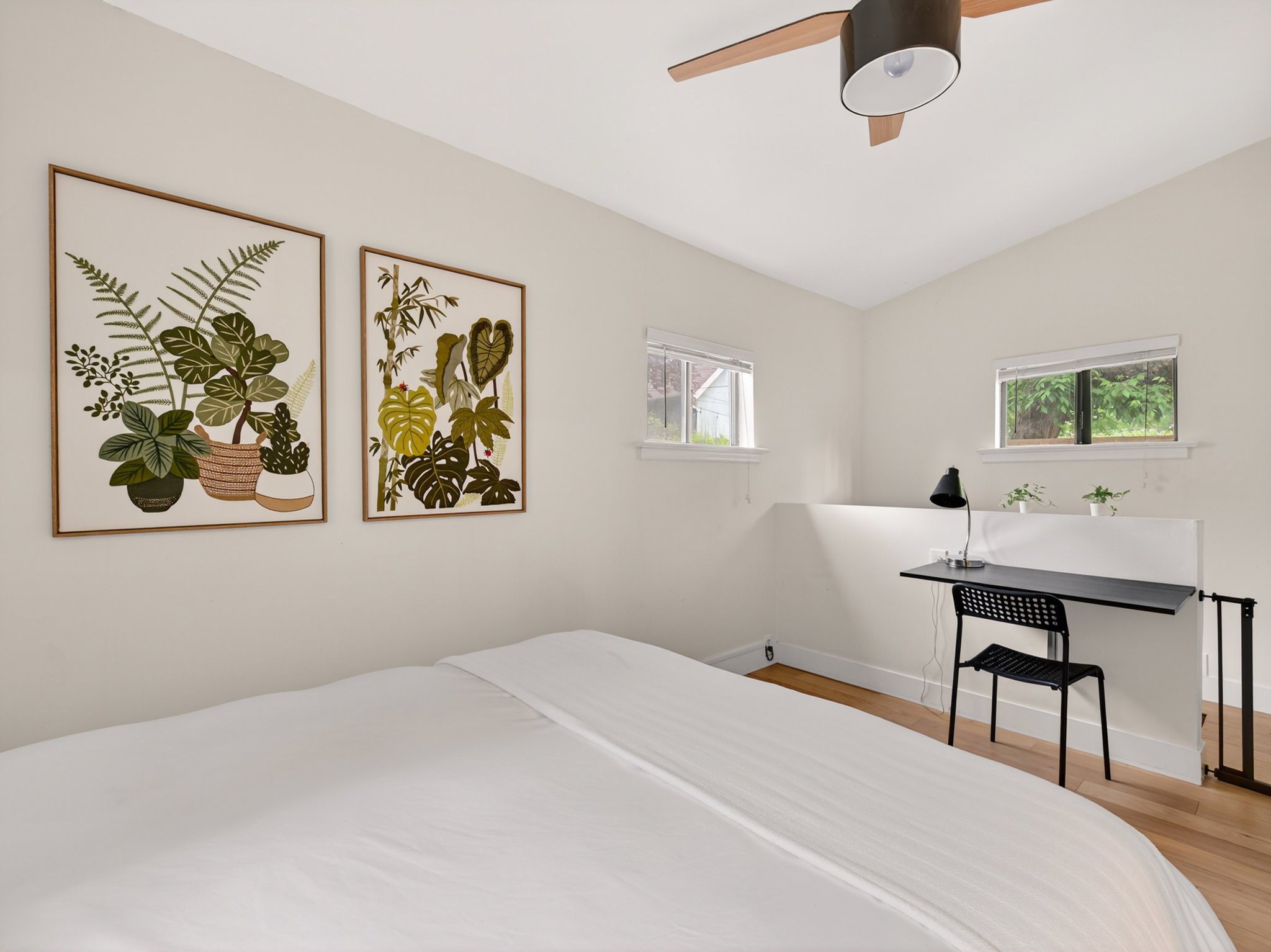 Bright room featuring wood-finish flooring, two large windows, a built-in desk, and a ceiling fan with light fixture