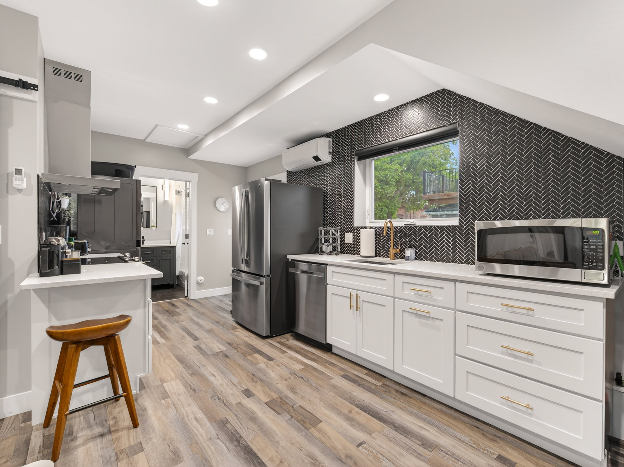 Kitchen featuring wood-finish flooring, white cabinetry with gold-tone hardware, a herringbone pattern accent wall, stainless steel appliances, and recessed lighting