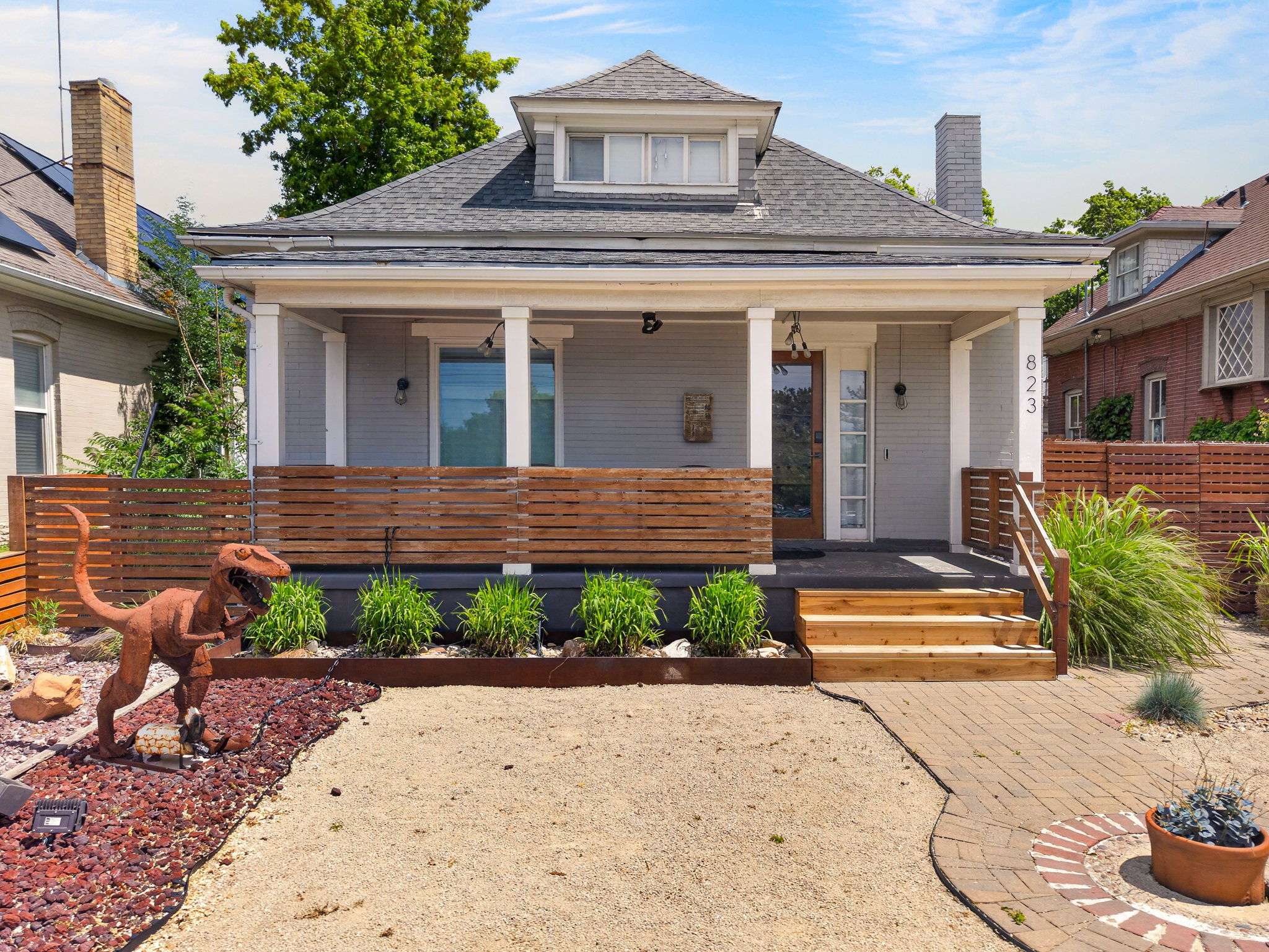 Gable-front bungalow featuring a covered porch with white columns, wood privacy screening, and a brick paver pathway