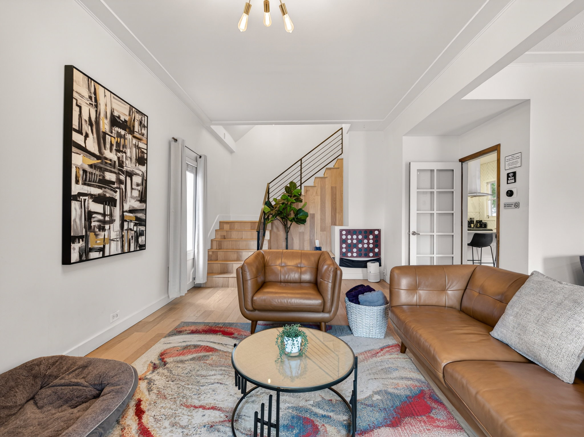 Bright living space featuring light wood-finish flooring, a modern open-tread staircase with metal railing, and a multi-pane glass door
