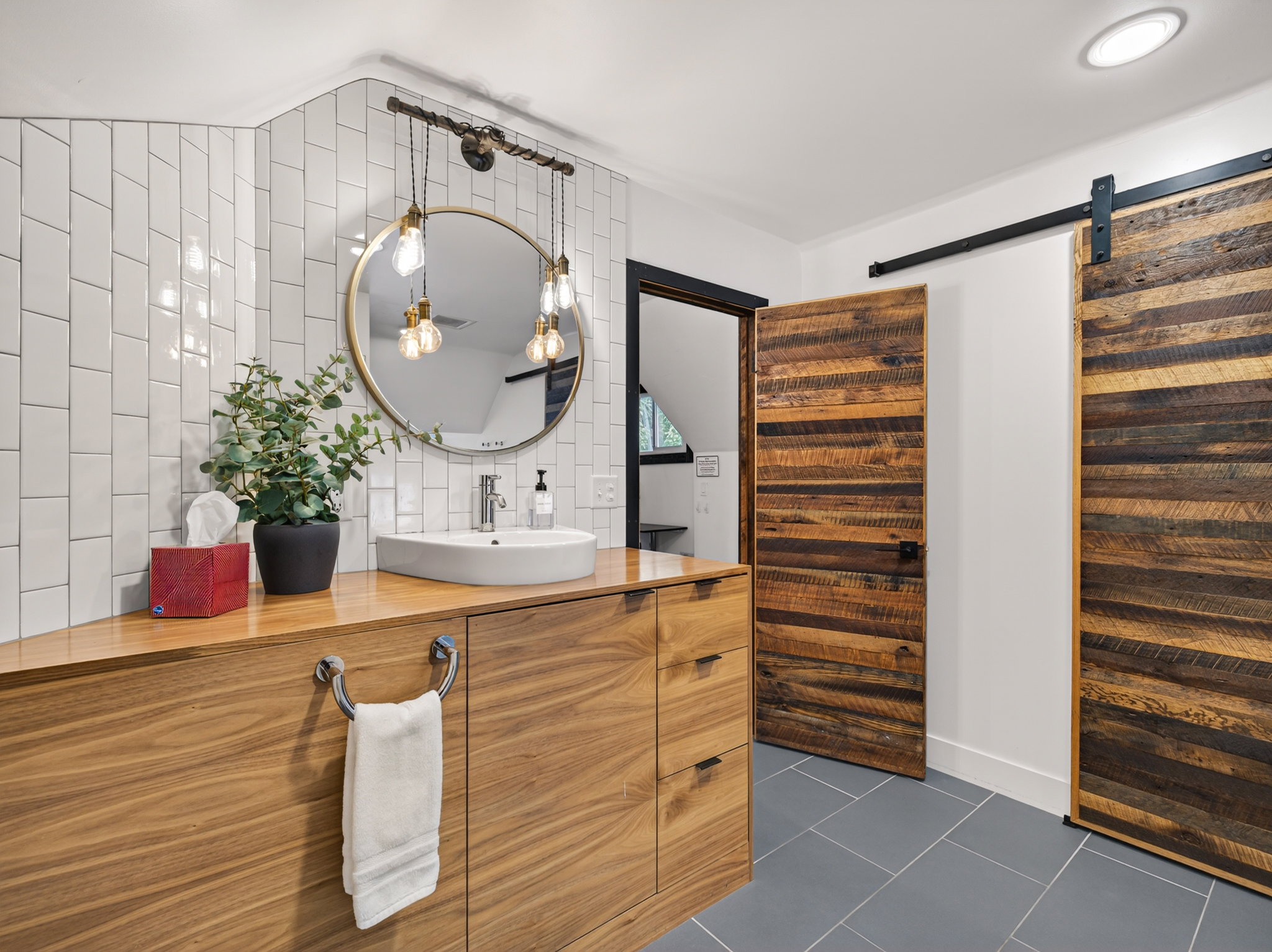 Bathroom featuring a wood-finish vanity with a vessel sink, a round mirror, and a three-bulb vanity light fixture