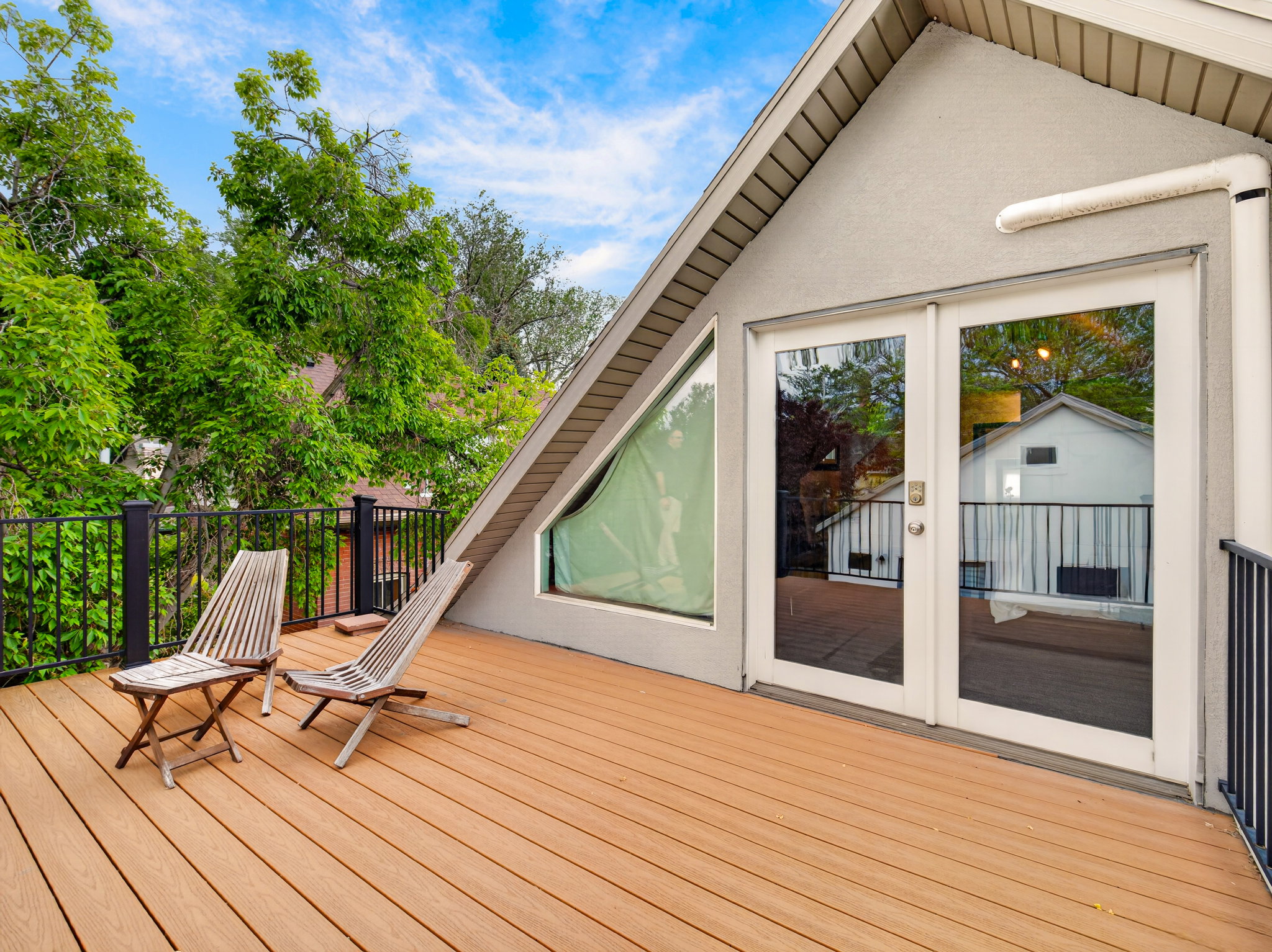 Expansive outdoor deck featuring wood-finish flooring, black metal railing, and a stucco exterior with a prominent A-frame architectural element