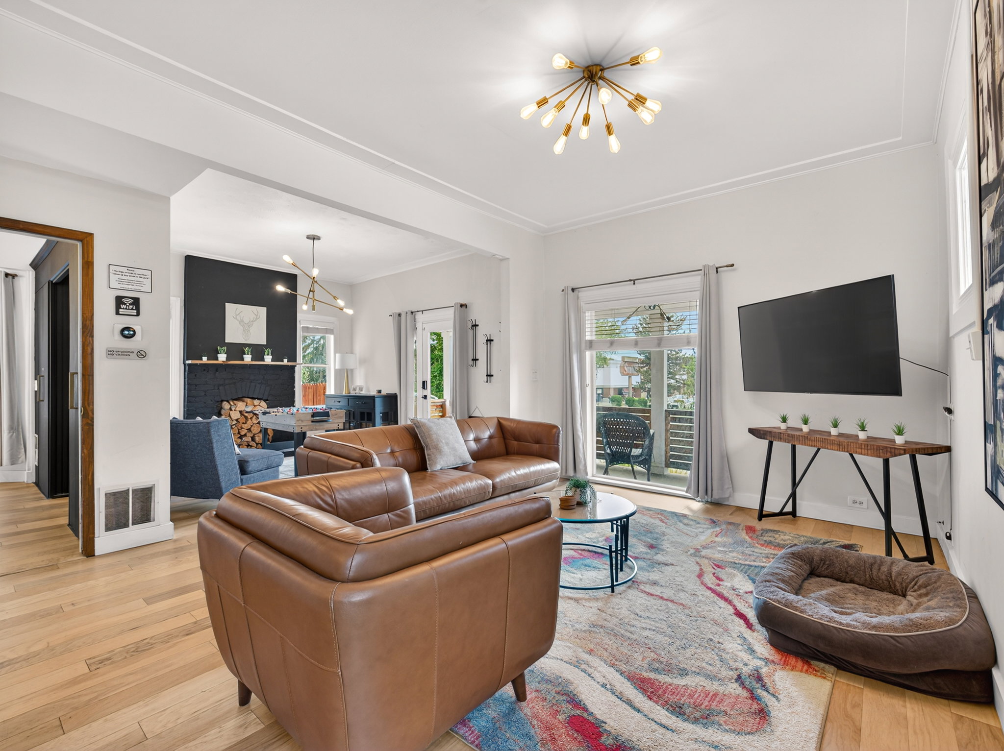 Spacious living area featuring light wood-finish flooring, a contemporary sputnik chandelier, and a decorative fireplace with a black brick hearth