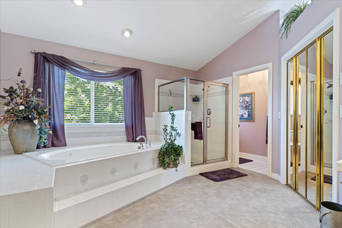 Soaking tub with tiled surround, glass-enclosed shower, vaulted ceiling, recessed lighting, and mirrored closet doors