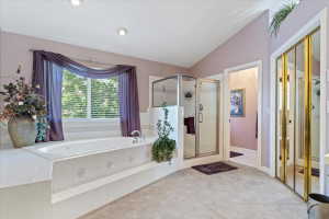 Soaking tub with tiled surround, glass-enclosed shower, vaulted ceiling, recessed lighting, and mirrored closet doors