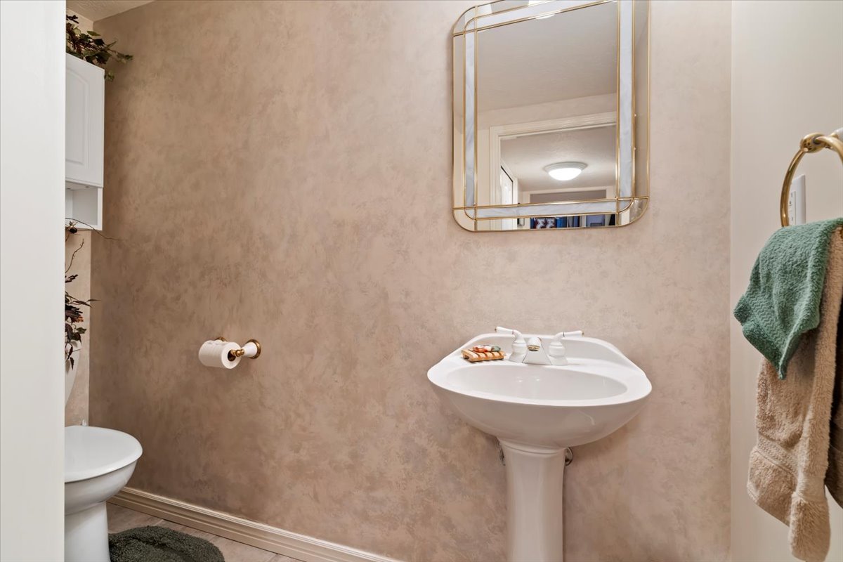 Pedestal sink with white faucet fixtures, framed mirror, and textured wall finish