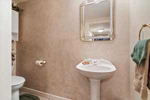 Pedestal sink with white faucet fixtures, framed mirror, and textured wall finish