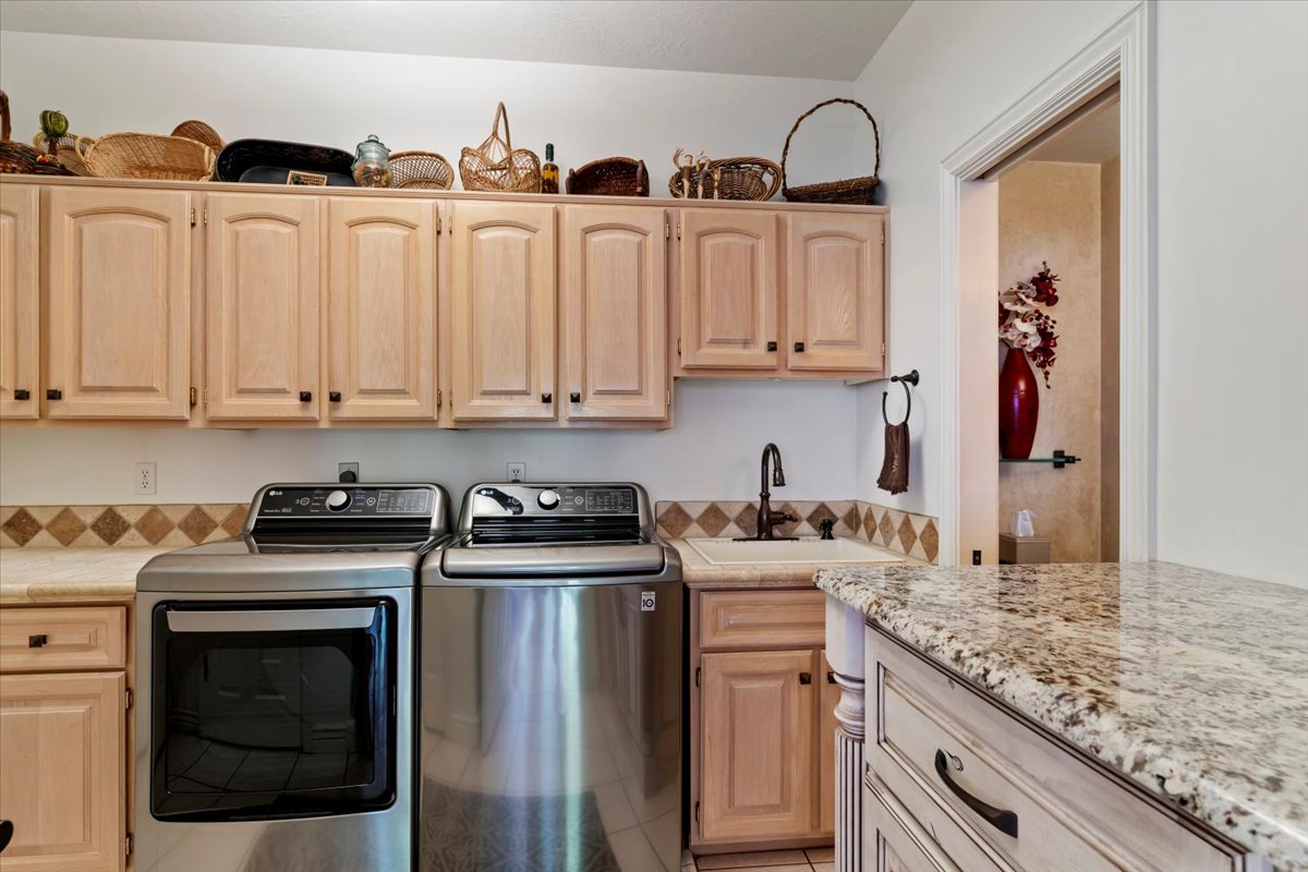 Dedicated utility space featuring extensive light wood-finish cabinetry, a built-in sink with a dark bronze-finish faucet, and granite-style countertops