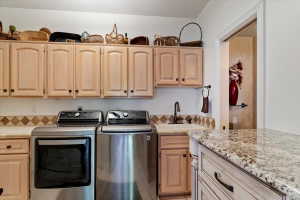 Dedicated utility space featuring extensive light wood-finish cabinetry, a built-in sink with a dark bronze-finish faucet, and granite-style countertops