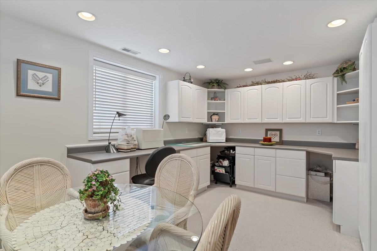 Bright room featuring extensive white cabinetry with upper and lower storage, a built-in desk area, recessed lighting, and a window with horizontal blinds