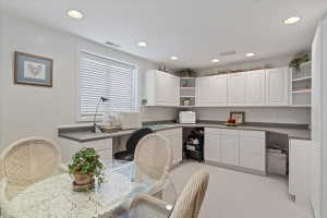 Bright room featuring extensive white cabinetry with upper and lower storage, a built-in desk area, recessed lighting, and a window with horizontal blinds