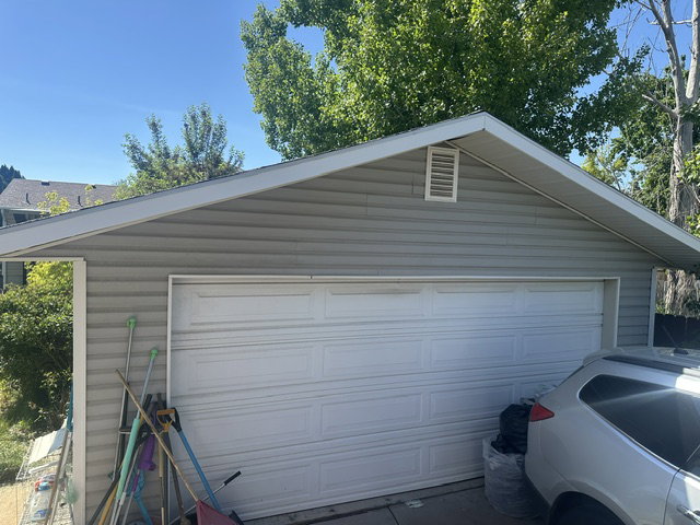 Detached garage featuring white panel garage door, light grey siding, and a gabled roofline with white trim