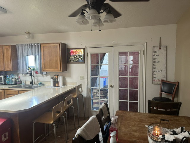 Kitchen featuring a peninsula countertop with seating, wood-finish cabinetry, a double basin sink with a gooseneck faucet, and French doors with privacy coverings