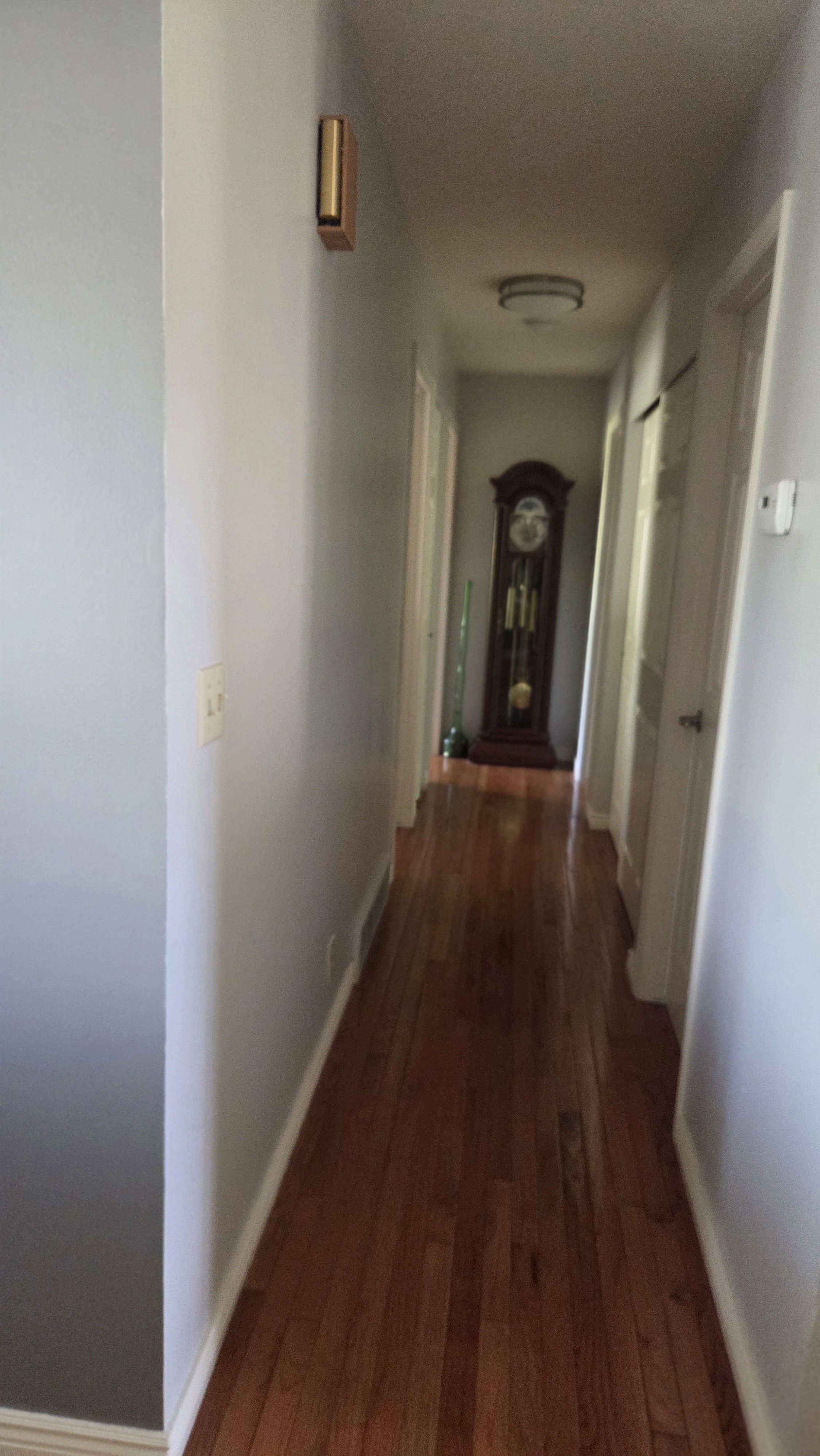 Hallway featuring wood-finish flooring, light grey painted walls, and white baseboards