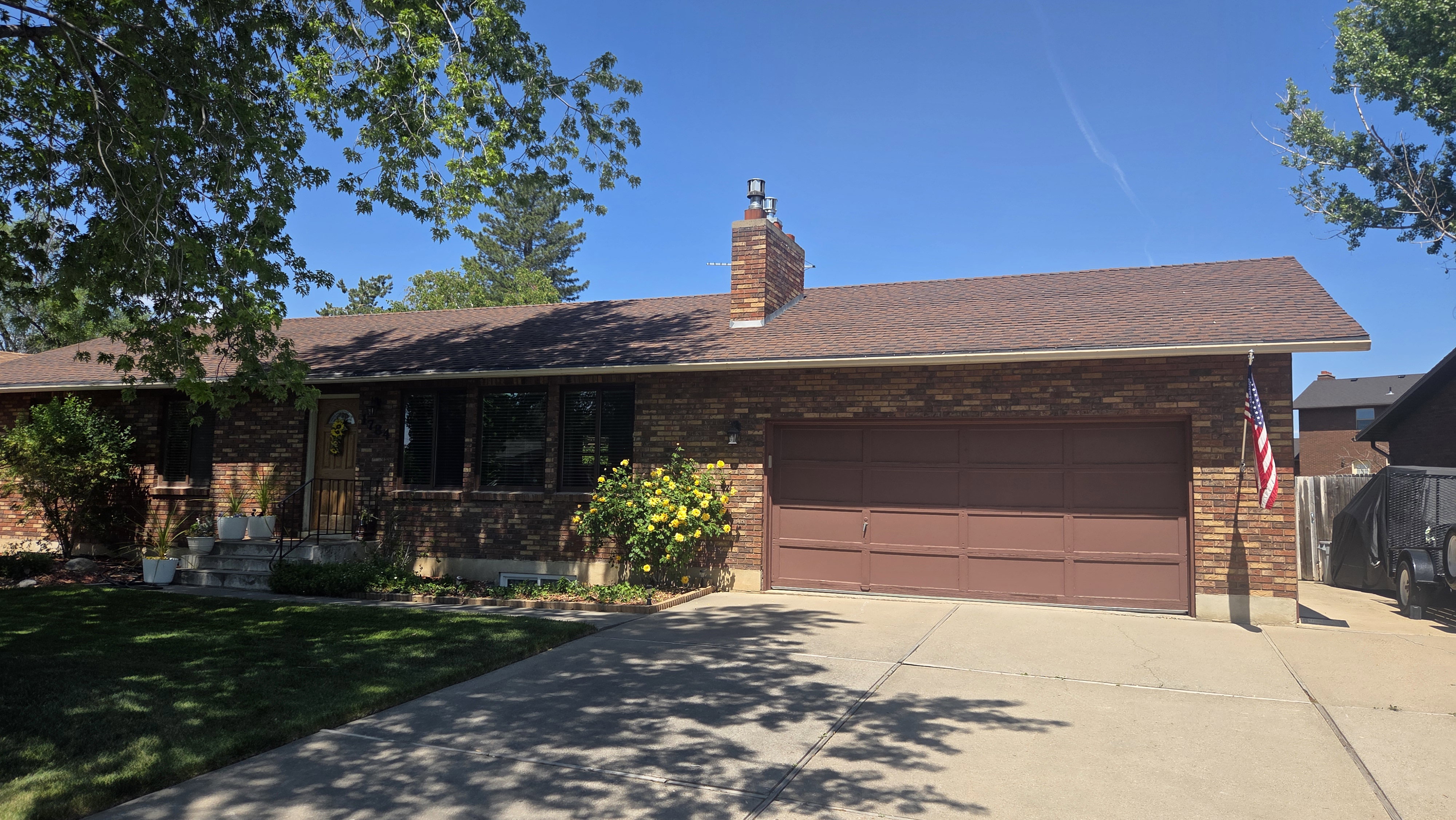 Brick exterior featuring an attached two-car garage, concrete driveway, and mature landscaping