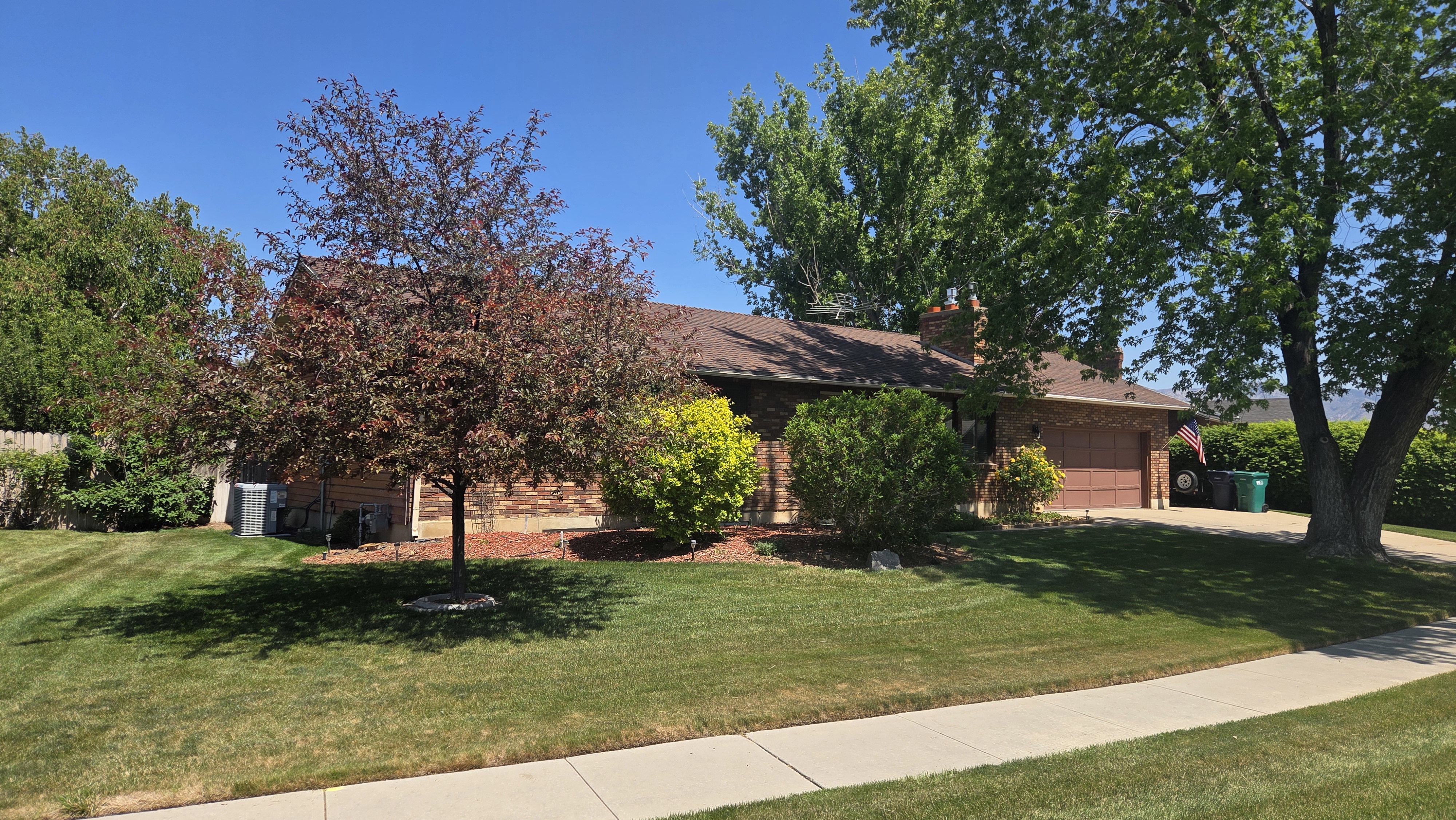 Brick exterior residence with an attached garage, featuring a shingle roof and mature trees providing shade