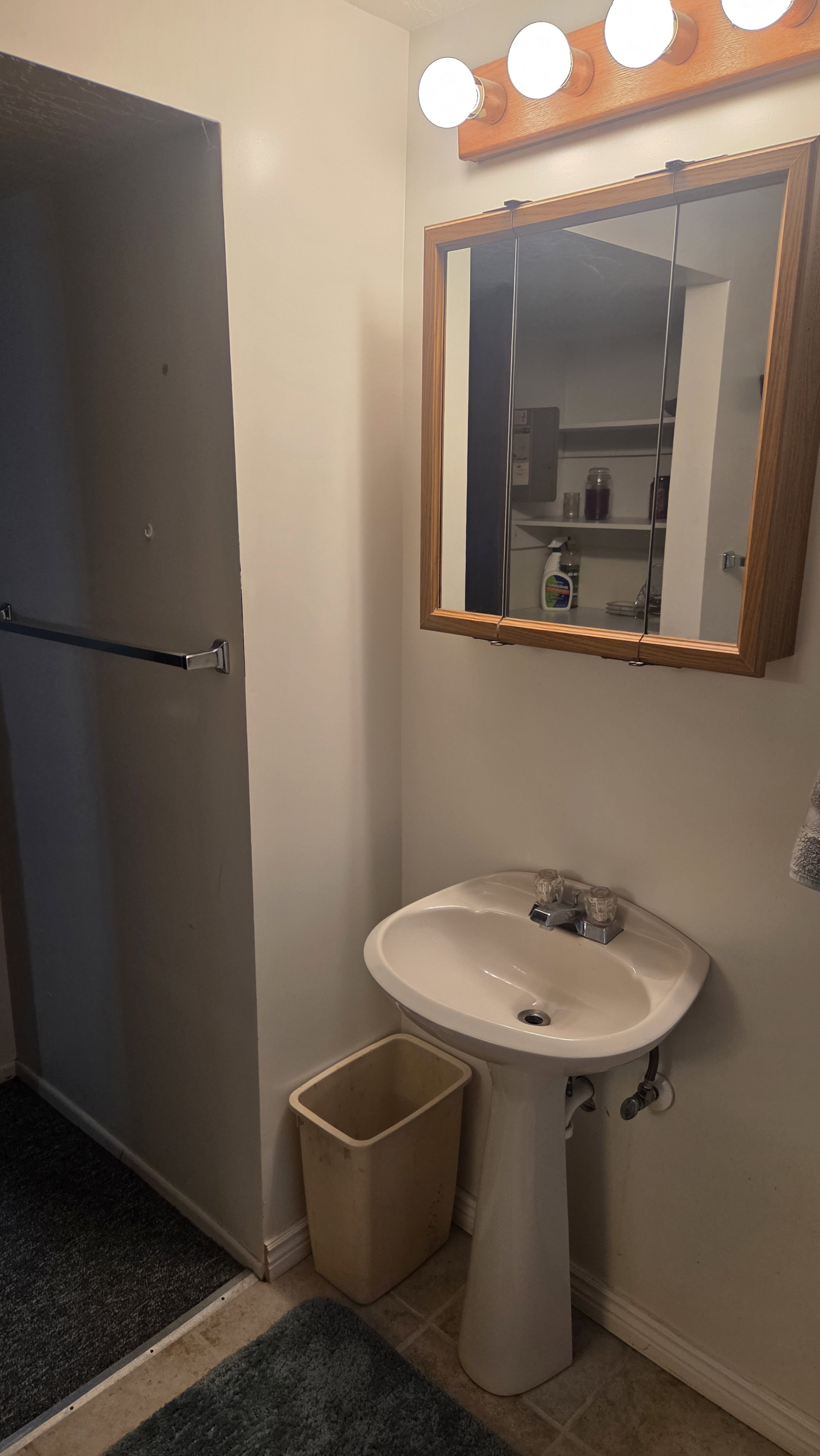 Pedestal sink with chrome fixtures, complemented by a wood-framed medicine cabinet and a four-bulb vanity light fixture