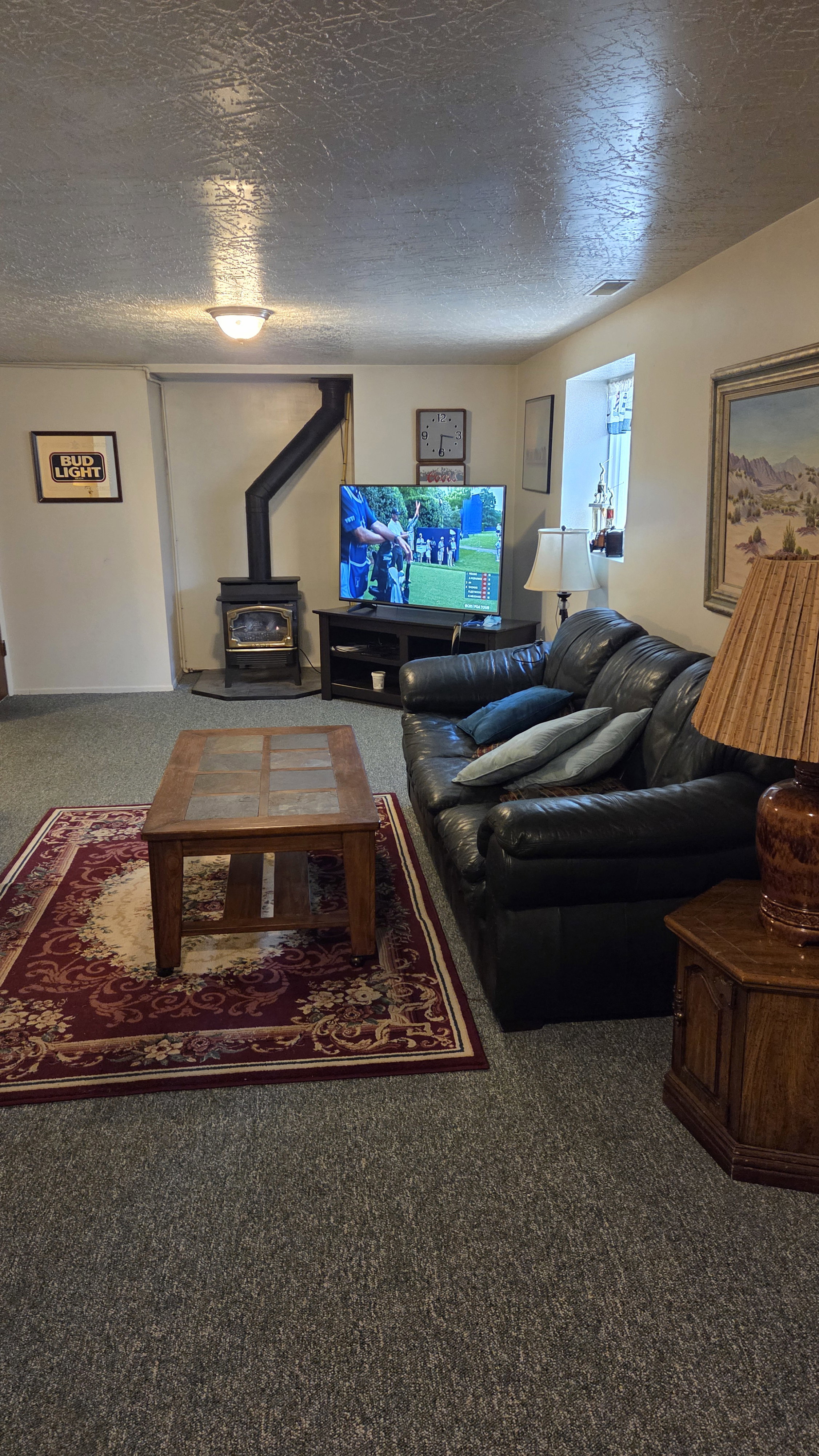 Living area featuring a wood-burning stove with black piping, a window with an interior sill, neutral wall paint, and textured ceiling