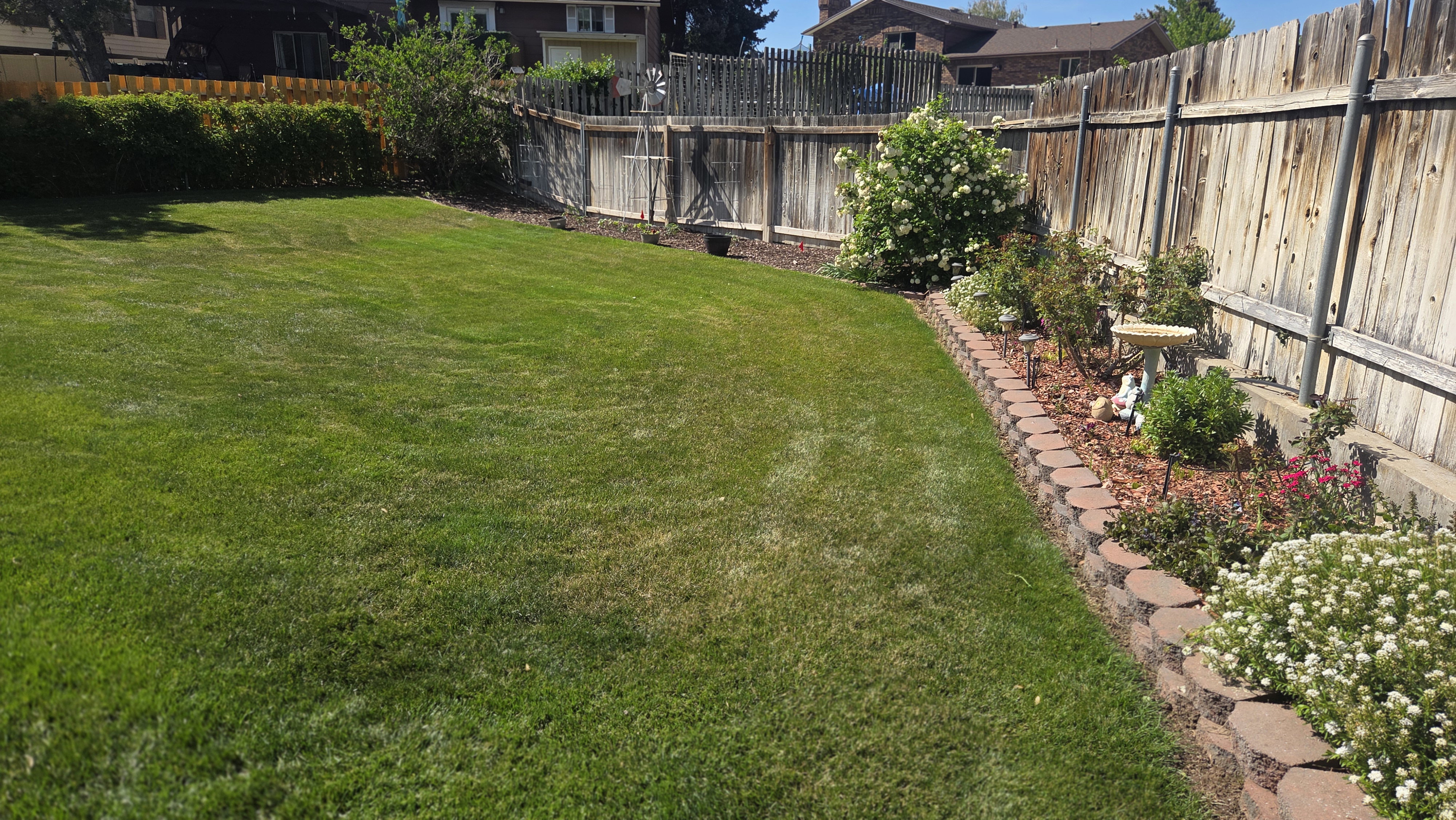 Expansive lawn area with a decorative retaining wall and mature landscaping, bordered by a wooden privacy fence