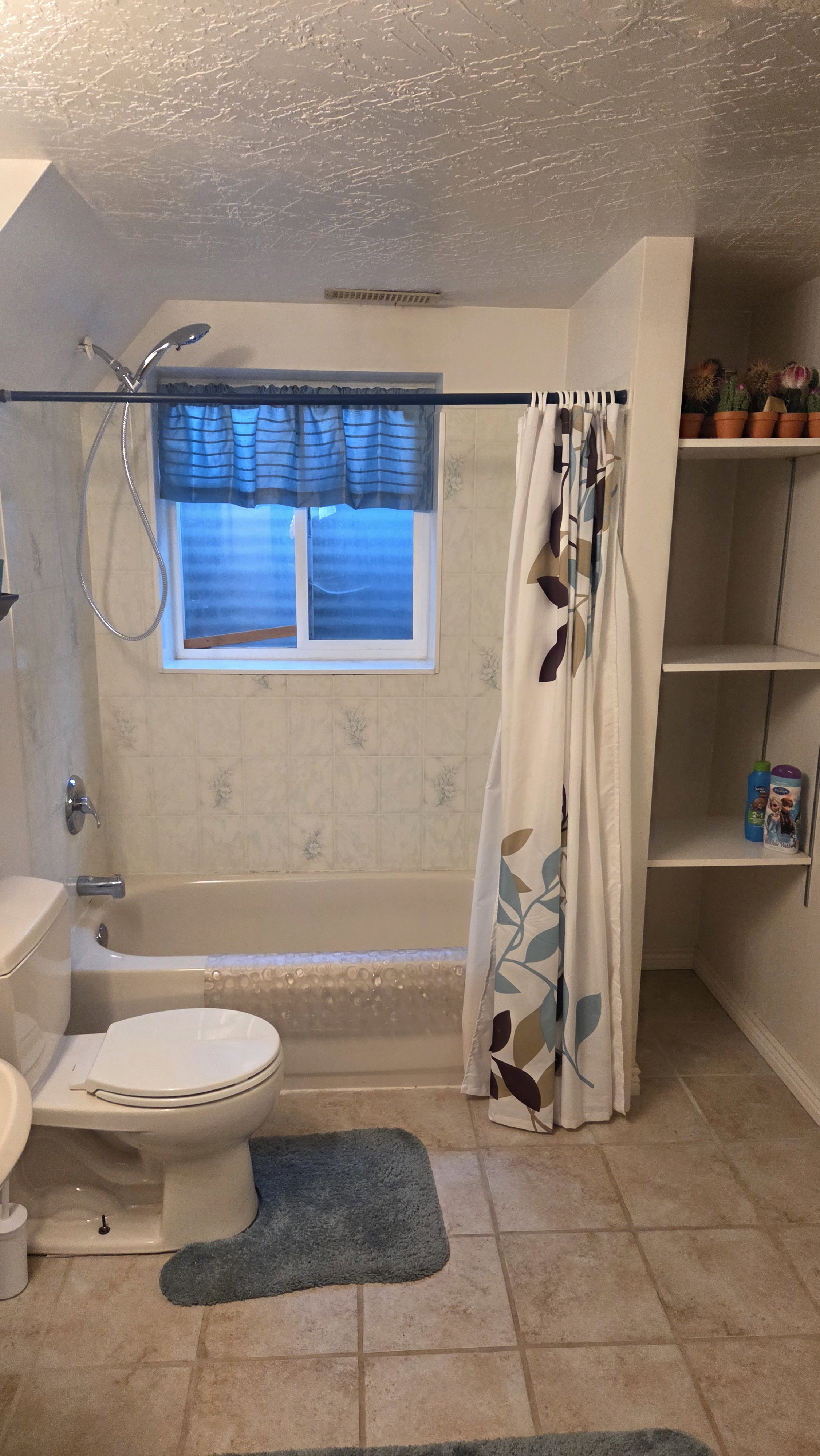 Full bathroom featuring a tub/shower combination with tiled surround, a window with privacy blinds, and built-in shelving