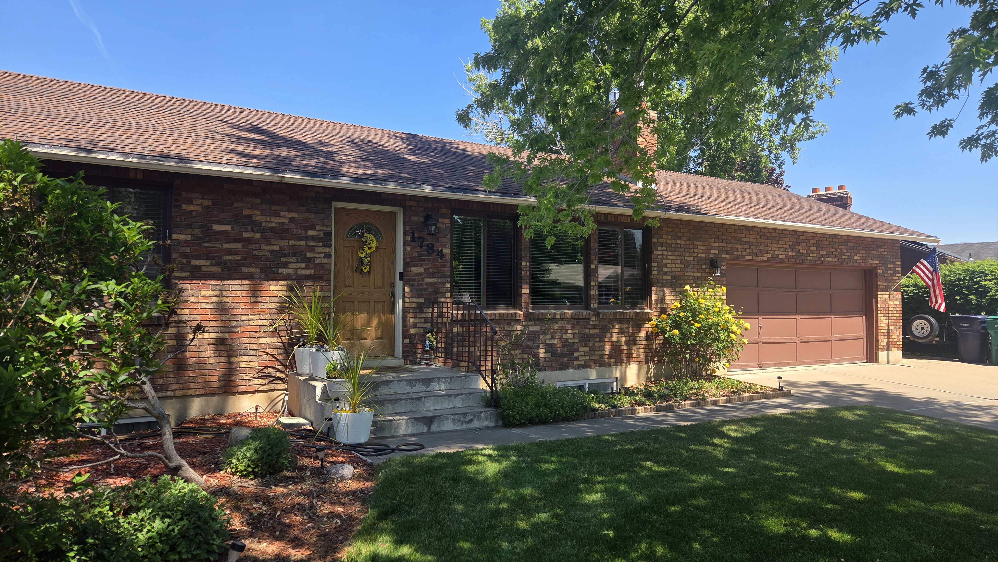Traditional brick exterior featuring a multi-pane front door, attached garage with a panel door, and mature landscaping