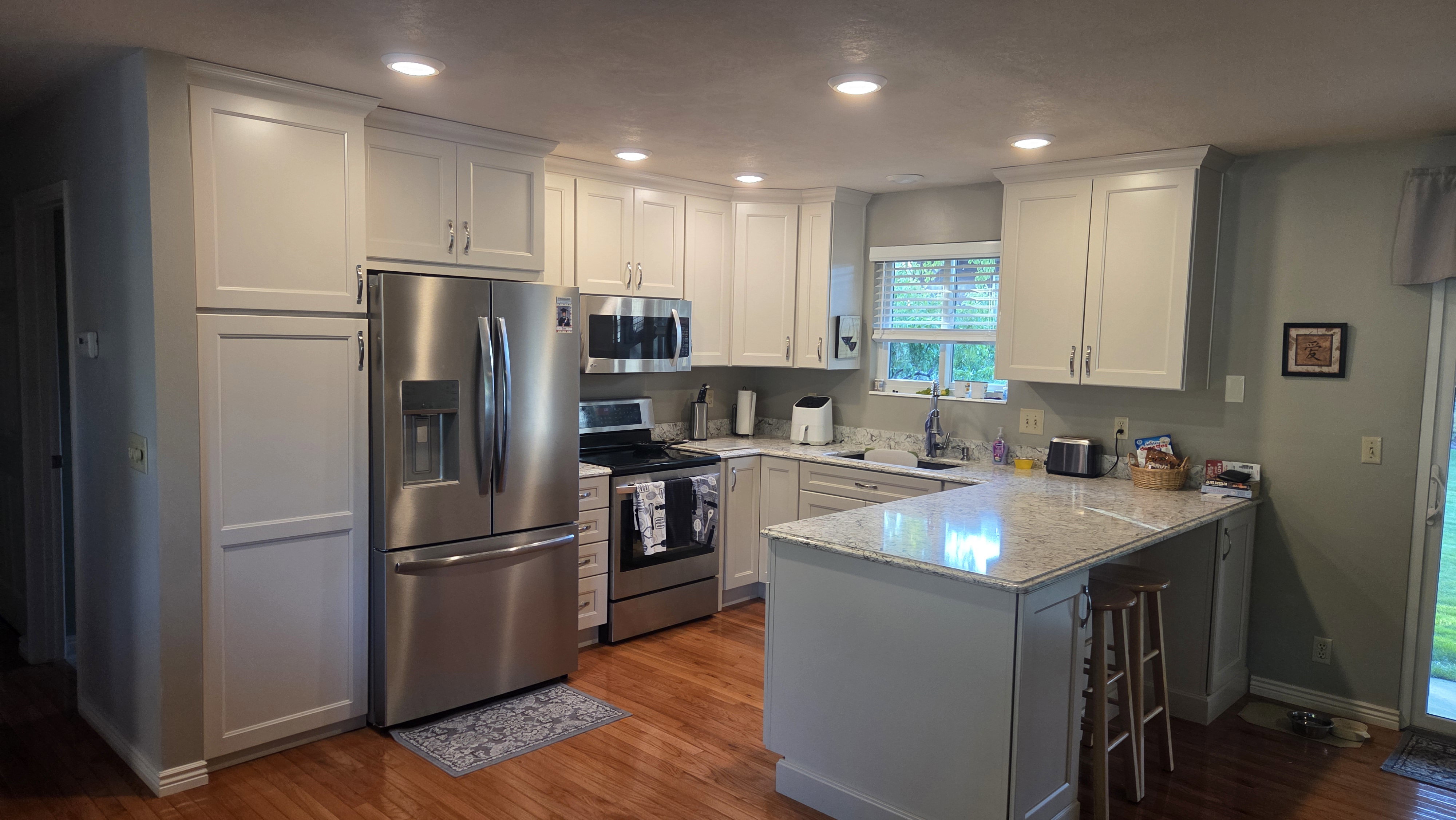 Kitchen featuring wood-finish flooring, recessed lighting, white shaker-style cabinetry, stainless steel appliances, and light-colored countertops with a breakfast bar