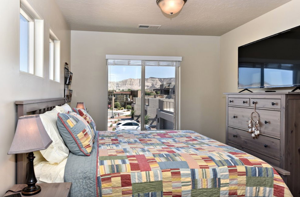 Bedroom featuring a full-light sliding glass door, a wall-mounted flat-screen display, and an adjacent window bank